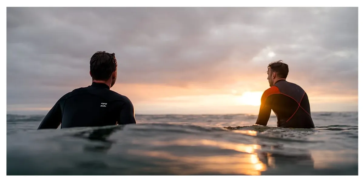 alt="Surfeur en combinaison entrant dans l&rsquo;eau pour une session de surf"